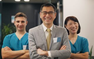 Business Man in front in suit and the with a male nurse to his left and a female nurse to his right with both nurses in blue scrubs